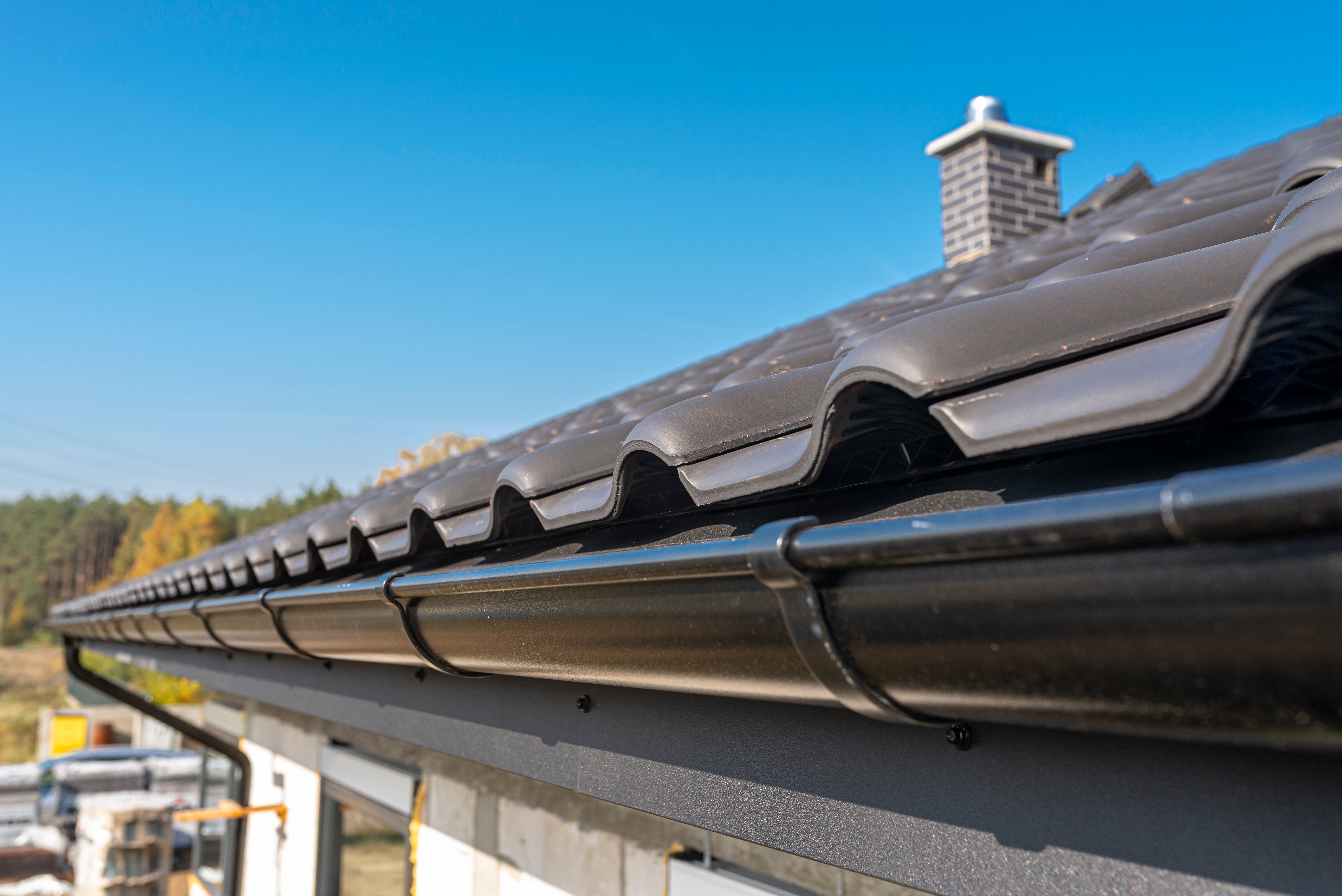 Black metal gutter installed along a tiled roof